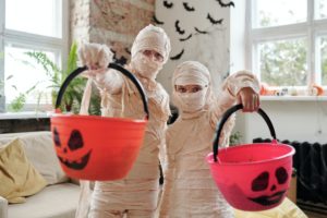 Two people dressed as mummies holding orange Halloween buckets with black printed faces