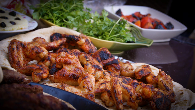 A dish of chicken wings with salad and fruit in the background